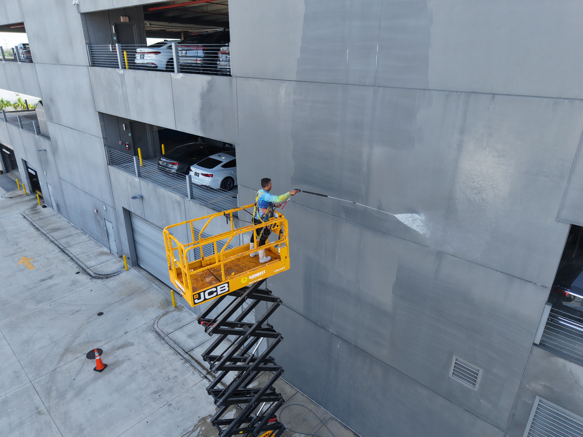 Worker on scissor lift cleaning multi-story building exterior in Hialeah FL