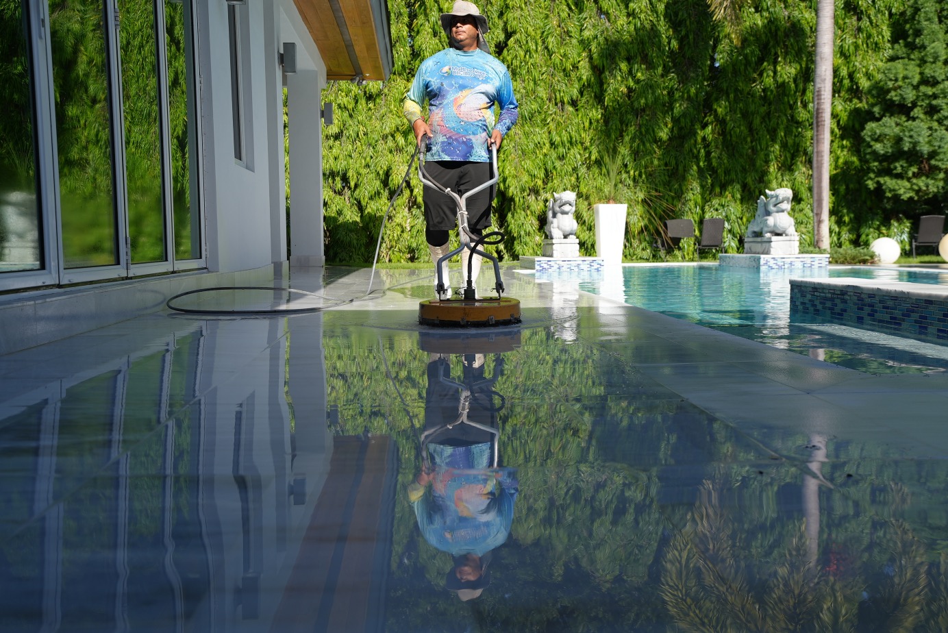 Worker with surface cleaner reflection on wet pool deck in Hialeah FL